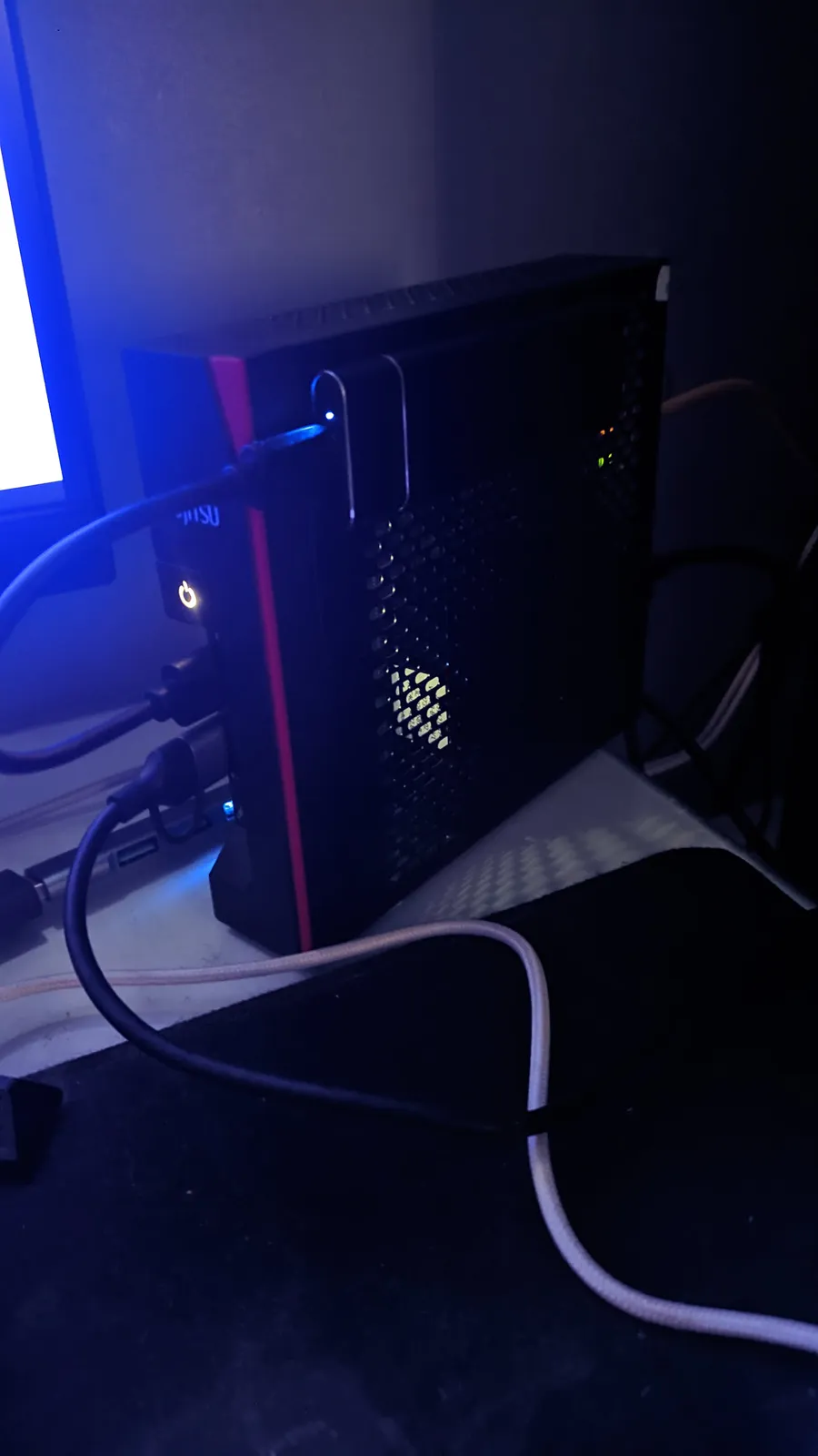 The small thin client that became the home server, lit by a monitor's blue glow